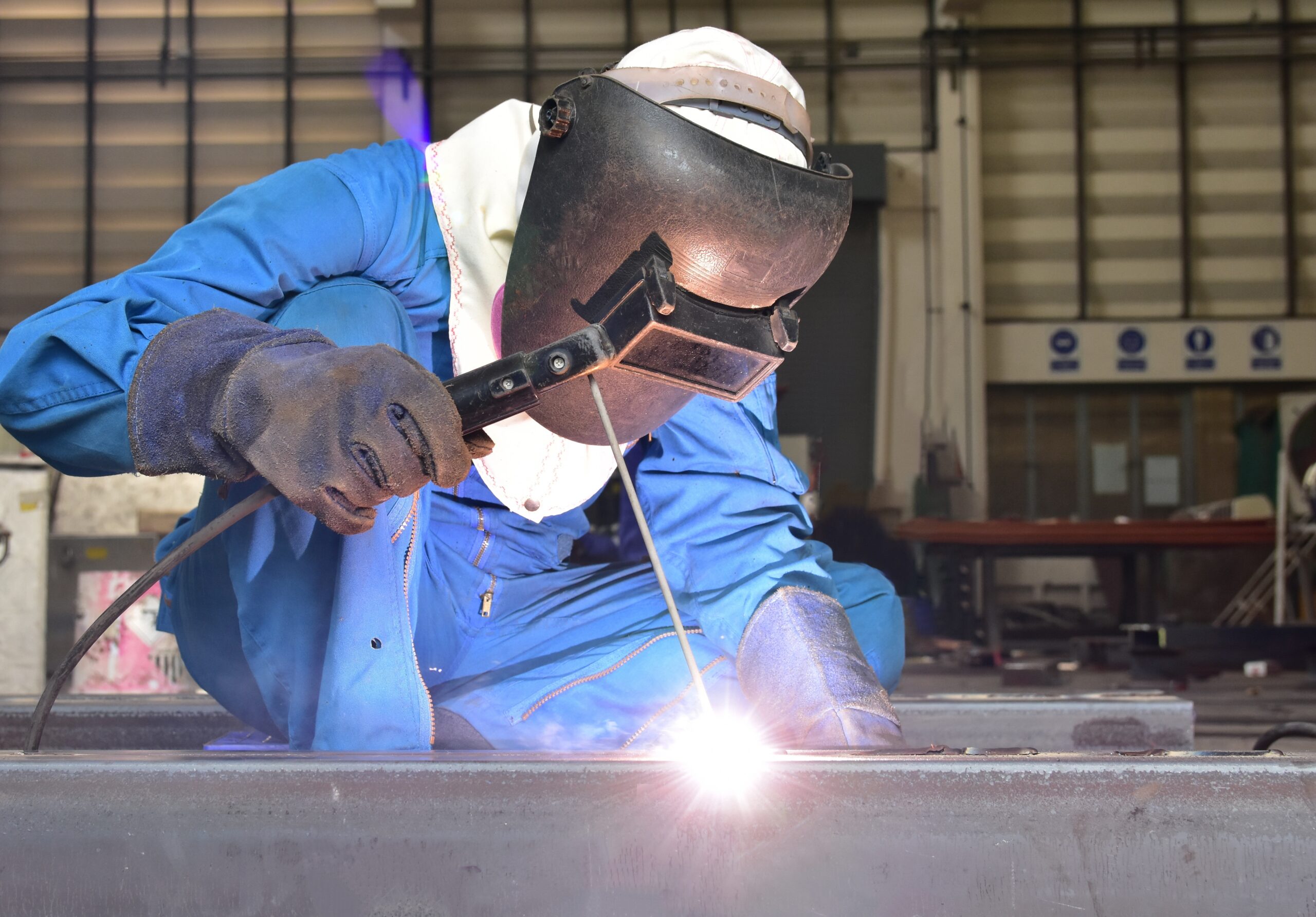 Welder performing precision welding on steel components in an industrial facility