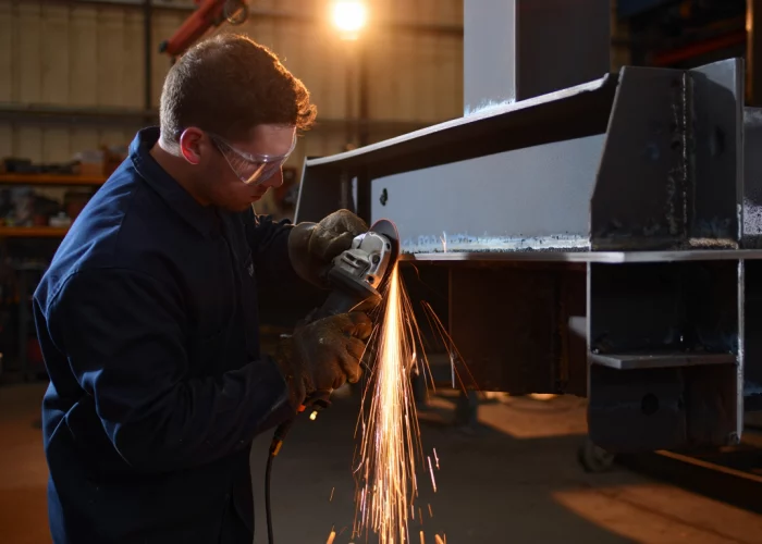 Industrial worker grinding a steel beam with an angle grinder in a fabrication workshop